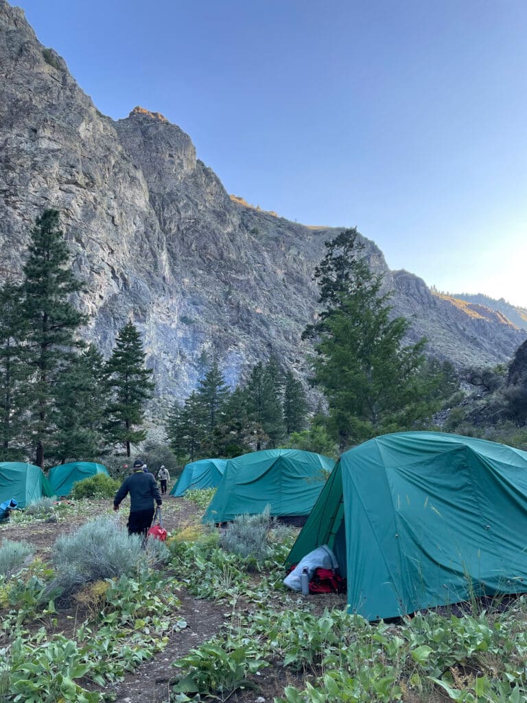 Middle Fork rafting essentials at a wilderness campsite with green tents set up beneath towering cliffs